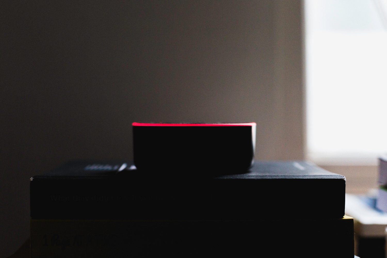 A side on photo of an Alexa Echo Dot, with a thin red glowing line around the rim, on top of some books.