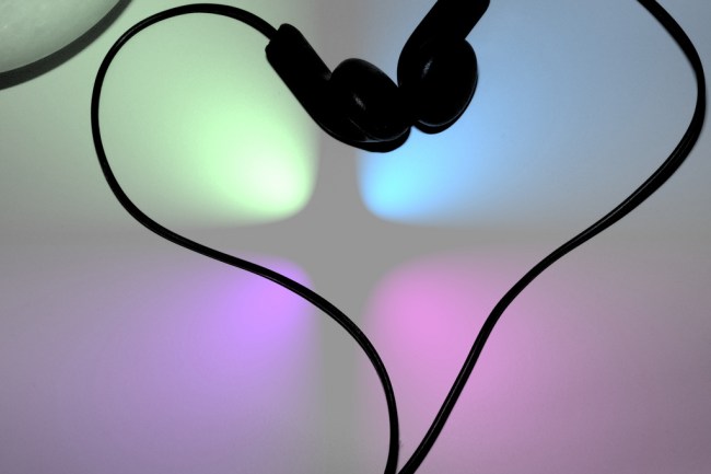 a photo of black in-hear bud headphones shaped into a heart, against a blurry background with 4 lights in a square (green, blue, purple, pink)