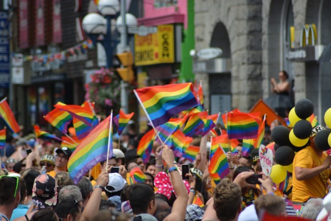 A Pride parade, a photo focused on lots of rainbow flags waving in the air above people's heads.