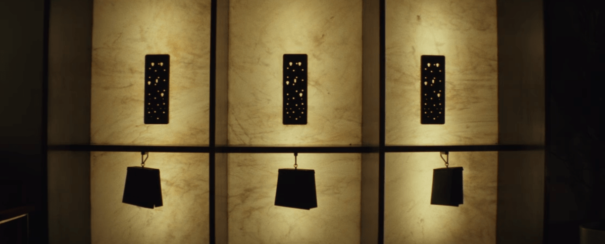 a photo of totally shadowed phone books hanging from chains under old phone operator banks, in three booths, backed by low lighting.