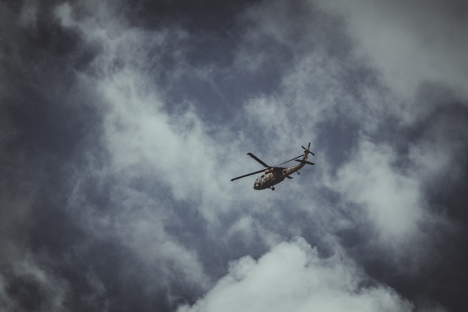 upward photo of a helicopter in the sky, surrounded by smoky clouds and dark grey blue sky.