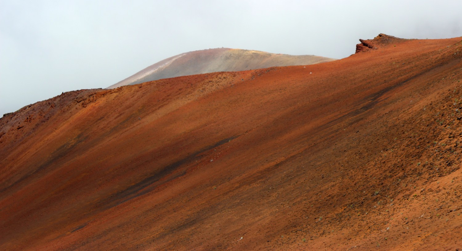 red desert landscape up a steep hill, with a grey cloudy sky above.