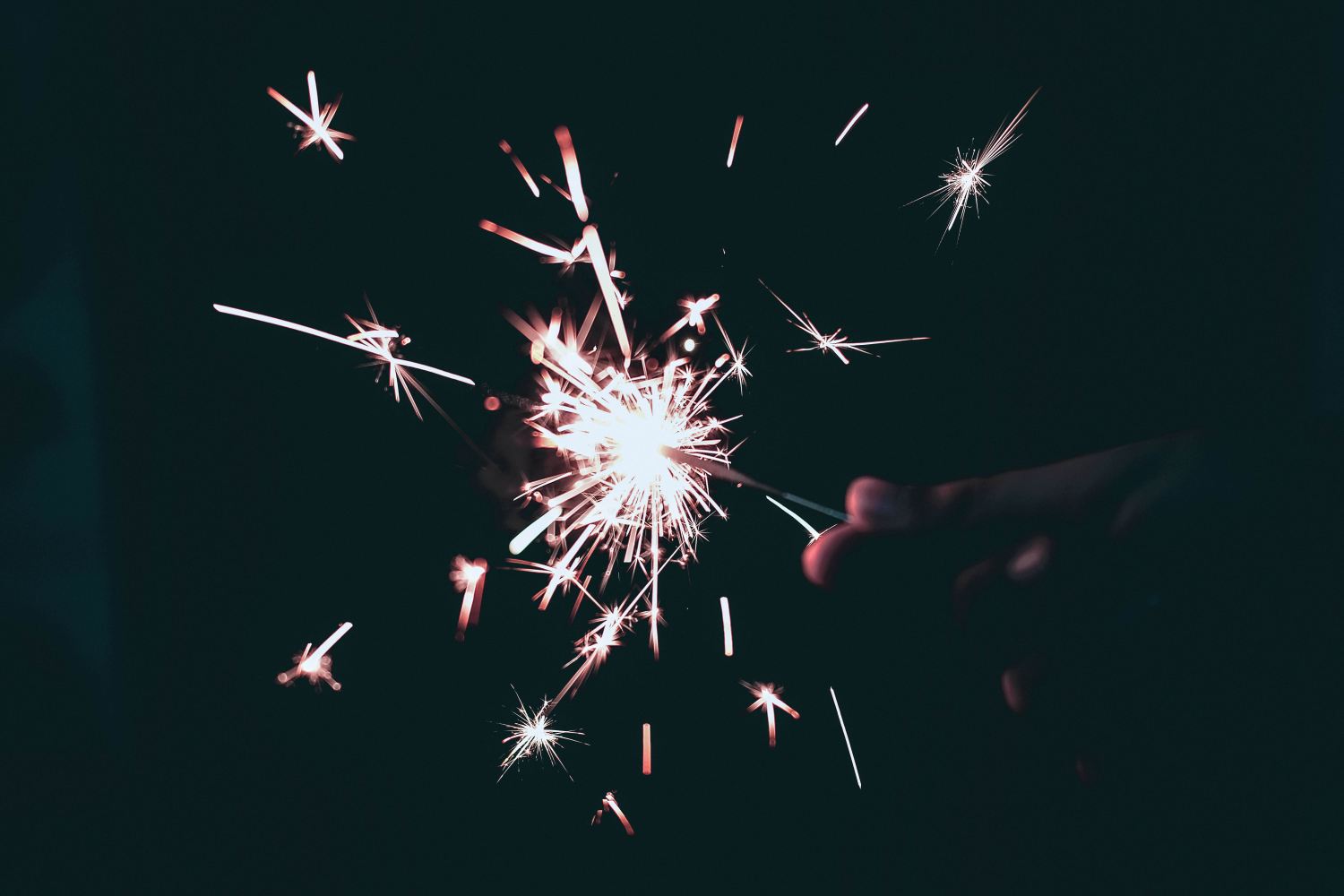 a hand holding a lit sparkler in the dark