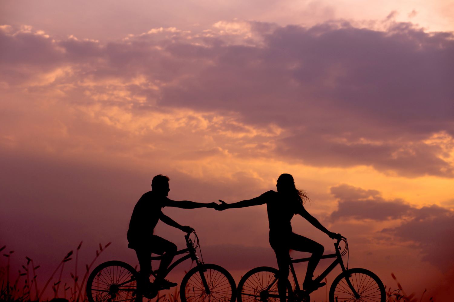 a biker reaching behind them to hold the hand of another biker at sunset